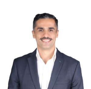 Portrait of a smiling man in a navy blazer and white shirt, looking at the camera on a plain background.